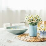 Stół z białym obrusem i kwiatkami w wazonie. Przykład stylu cottagecore