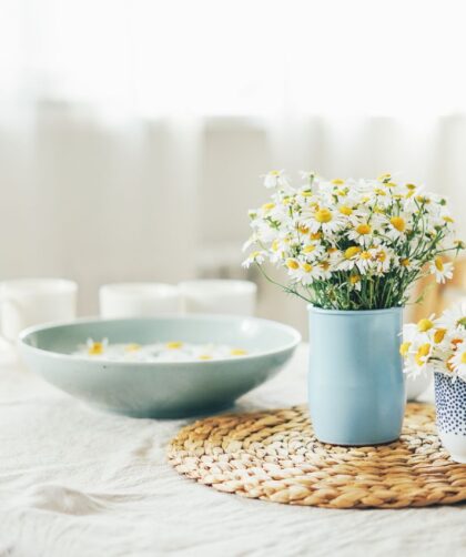 Stół z białym obrusem i kwiatkami w wazonie. Przykład stylu cottagecore